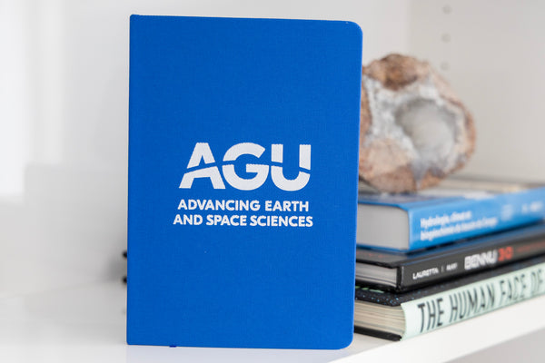 A blue notebook with the AGU logo in white is pictured in front of a short stack of books
