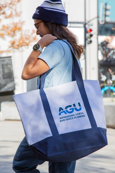 A woman wearing an AGU beanie carries a large zippered tote bag.