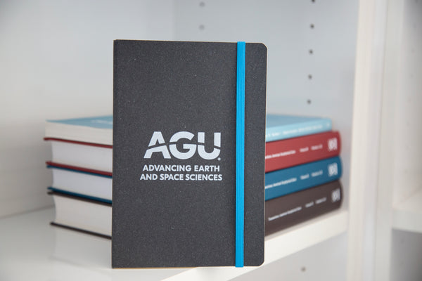 A dark grey notebook is shown. The notebook has a light blue elastic strap and the AGU logo printed in white.