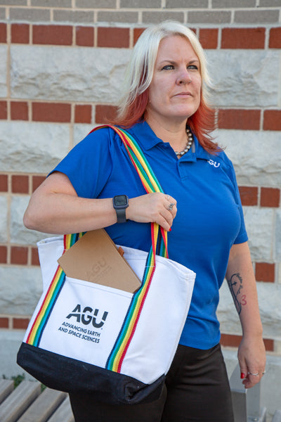 A woman wearing a blue AGU polo shirt holds a tote bag with the AGU logo