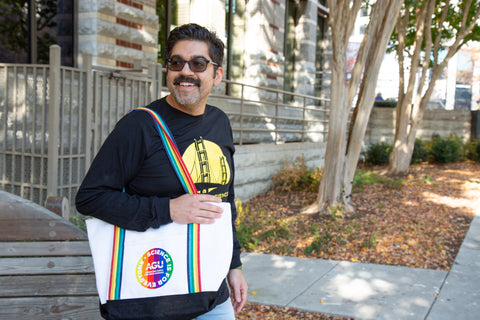 A man wearing the long-sleeve AGU23 t-shirt holds an AGU tote bag featuring Science is for Everyone