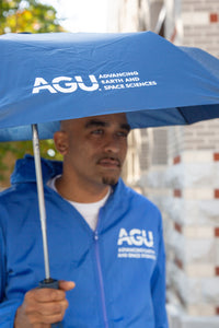 A man holds an open umbrella displaying the AGU logo