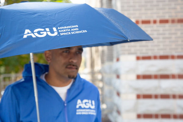 A man holds an open umbrella displaying the AGU logo