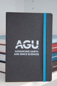 A dark grey notebook is shown. The notebook has a light blue elastic strap and the AGU logo printed in white.