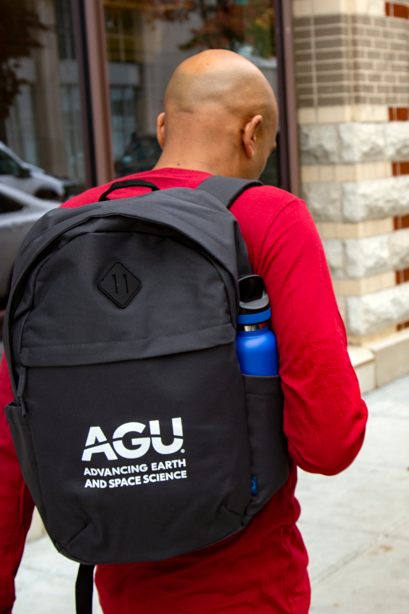 A man walks away from the camera, wearing a backpack with the AGU logo