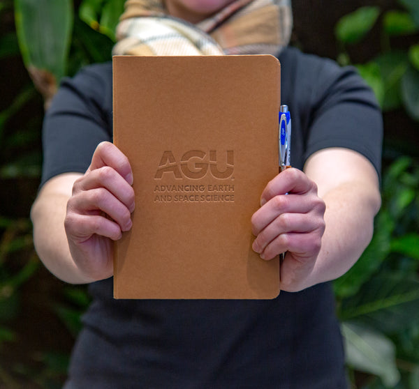 A person holds a notebook embossed with the AGU logo